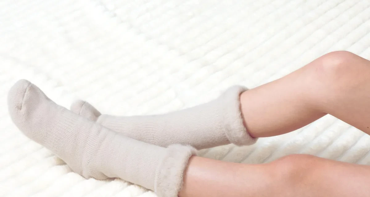 A pair of UnboxMe Sweet Dreams fuzzy cloud socks in mauve and stone, worn on a cream waffle blanket.